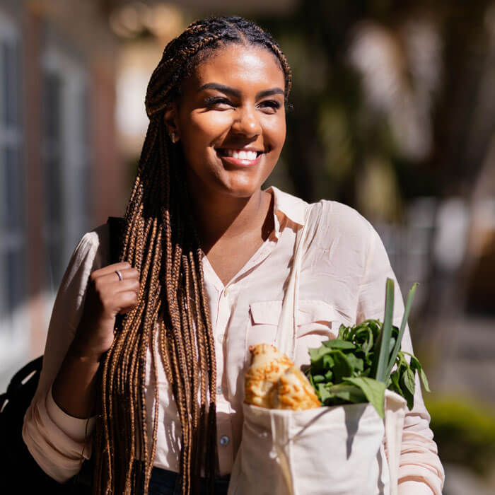 smiling young woman carrying a bag of groceries walking back to her home