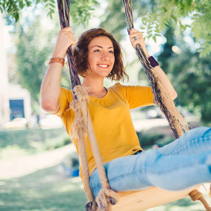 Happy woman swinging under a tree in a park