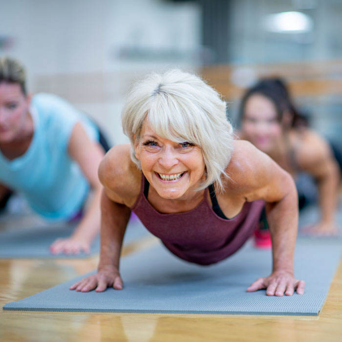 Mature woman is seen holding a plank pose while participating in a fitness class